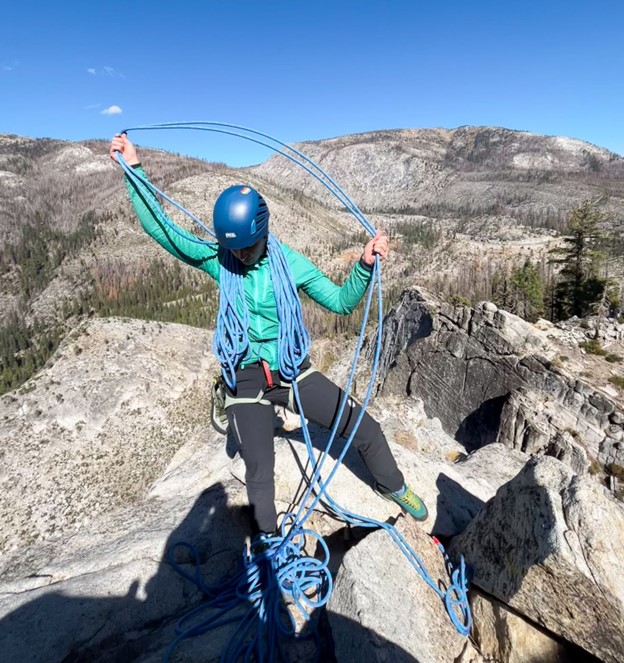 Woman climber coiling climbing rope in the mountains.