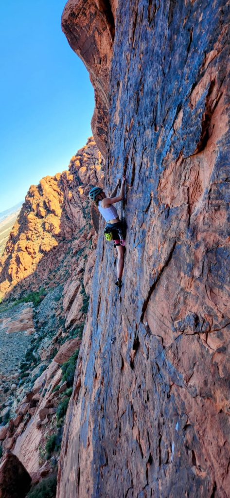Woman rock climber climbing large red rock outdoor wall.