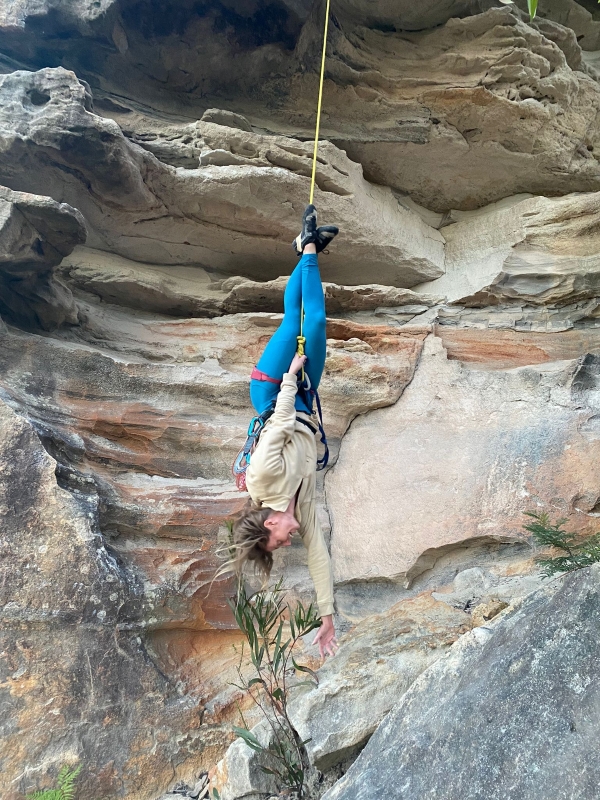 Woman having fun hanging upside down during outdoor rock climb.