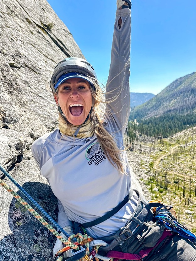Woman celebrating atop outdoor rock climb.
