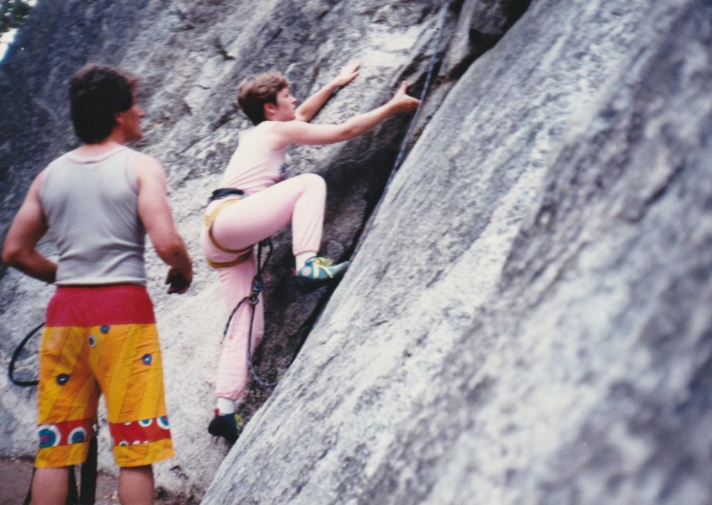 Woman rock climbing wearing pink tank top and sweat pants.