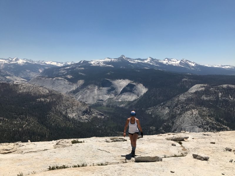 Woman hiking up granite with mountain landscape in the background.