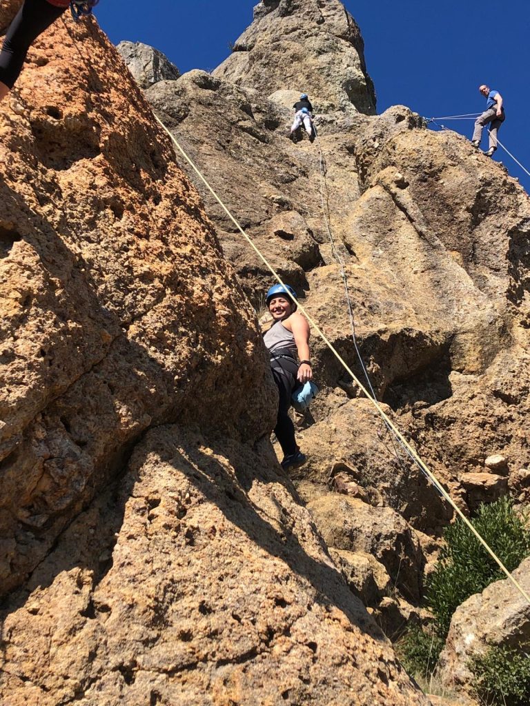 Woman smiling at the camera while rock climbing outdoors.