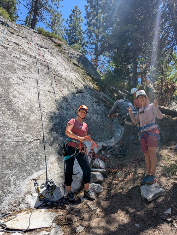 Two women wearing PPE and posed for portrait during a rock climbing safety class in front of granite rock wall.