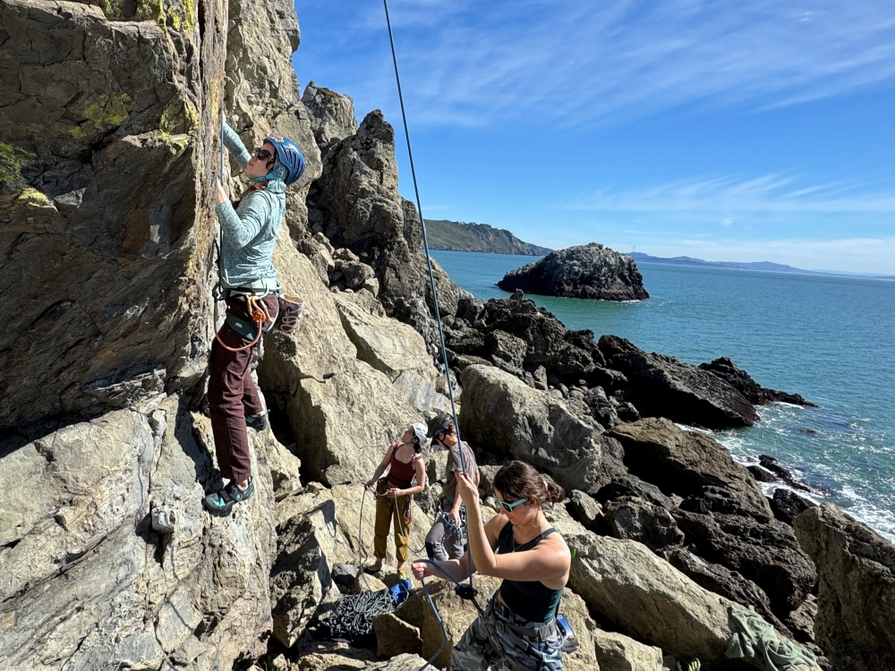 Women rock climbers climbing at coastal crag with ocean in the background.