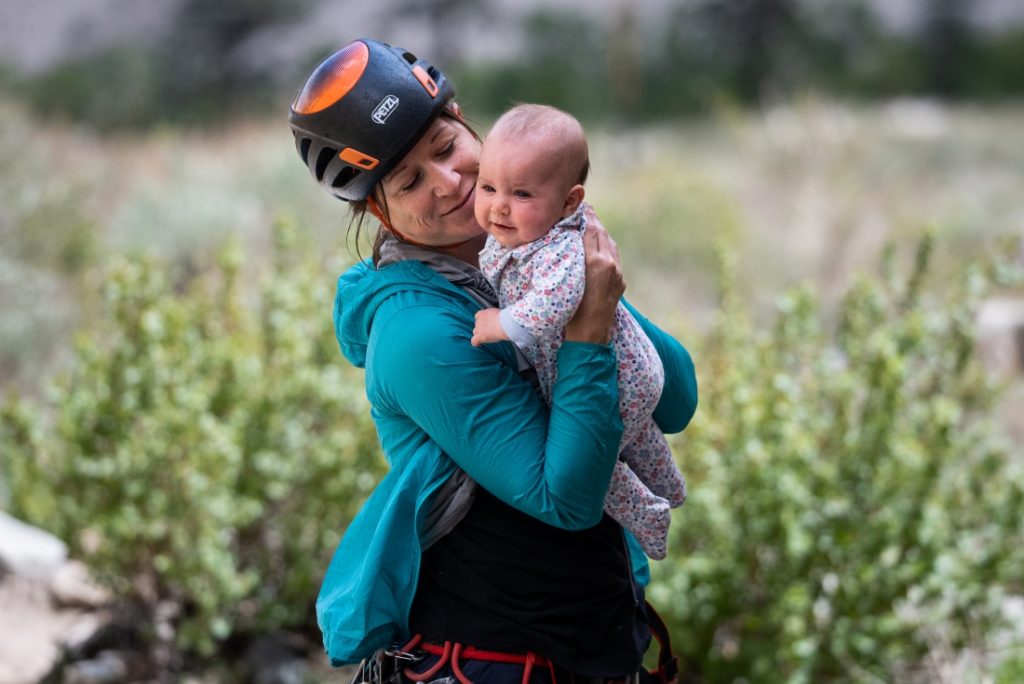 Woman rock climber holding baby girl and smiling at her.