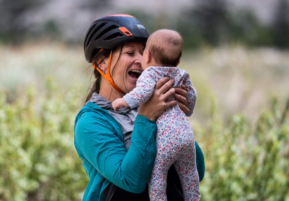 Woman rock climber holding baby girl an smiling at her.